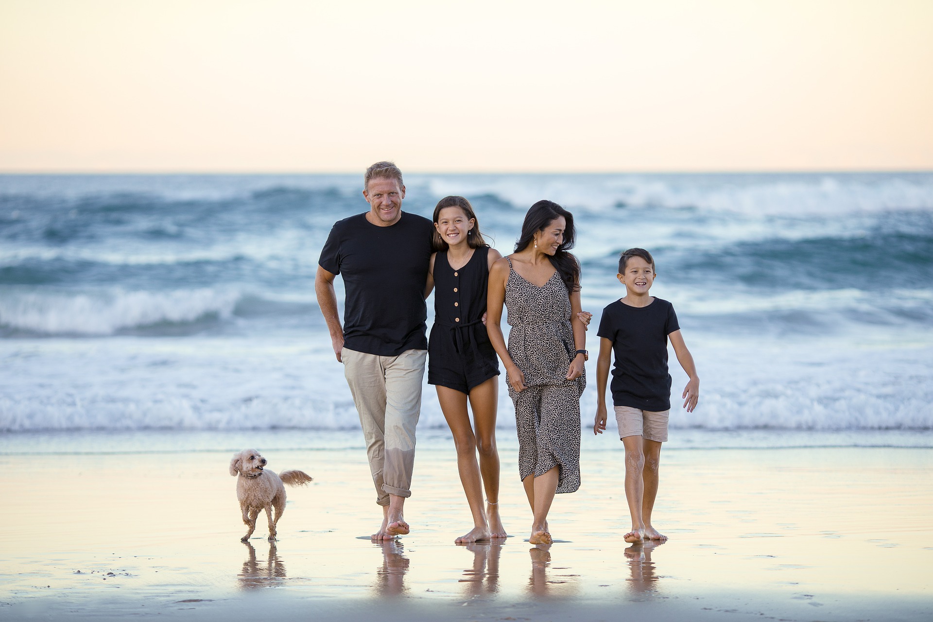family with dog walking on the beach, with ocean in background