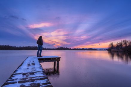 Man standing on dock in winter, overlooking water